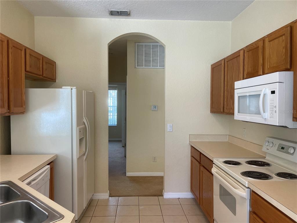 A kitchen with wood cabinets, white appliances, tile flooring, and an arched doorway — 1628 N HAMPTON DRIVE, DAVENPORT, FL