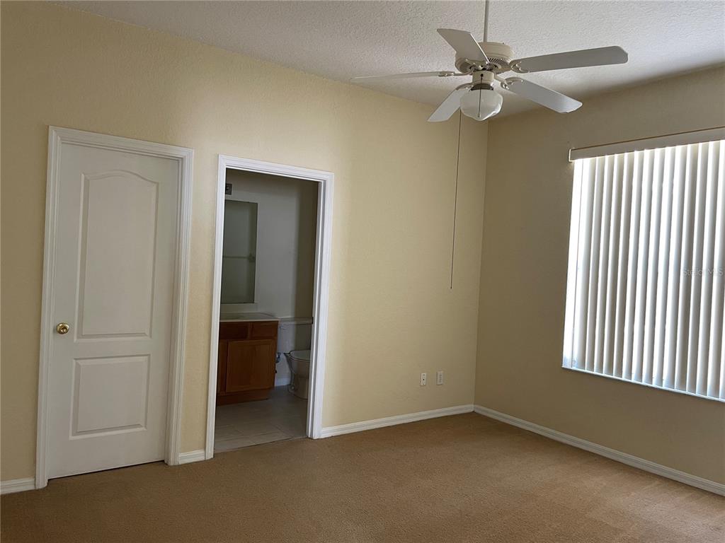 A bedroom with beige carpet, tan walls, a ceiling fan, and an attached bathroom — 1628 N HAMPTON DRIVE, DAVENPORT, FL