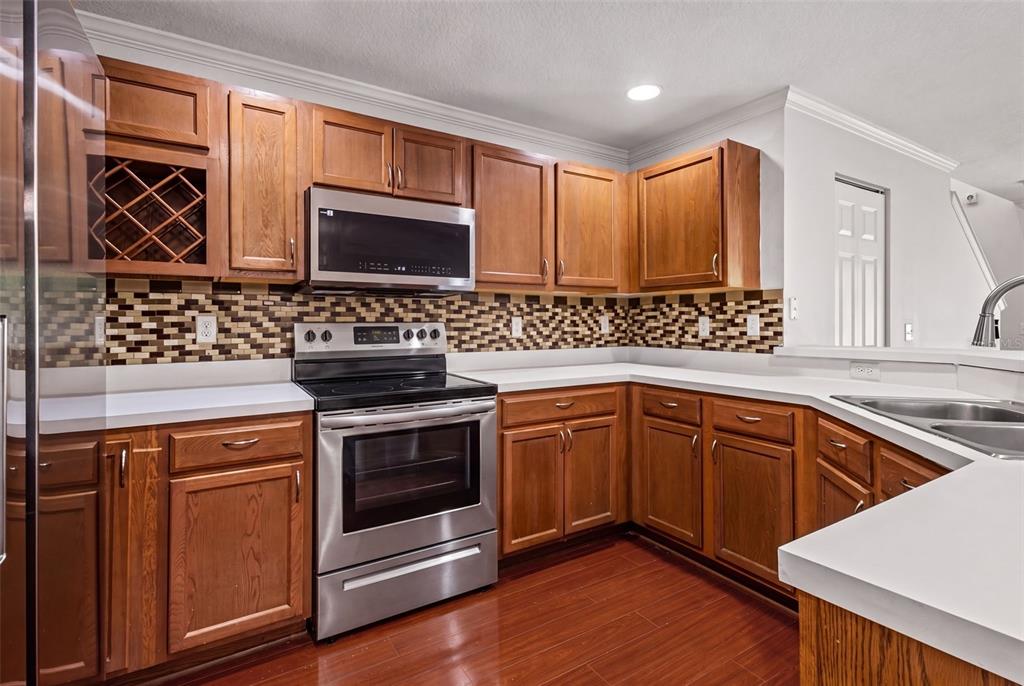 A kitchen with wood cabinets, white countertops, stainless steel appliances, and reddish-brown wood flooring — 2972 ROYAL TUSCAN LANE, VALRICO, FL