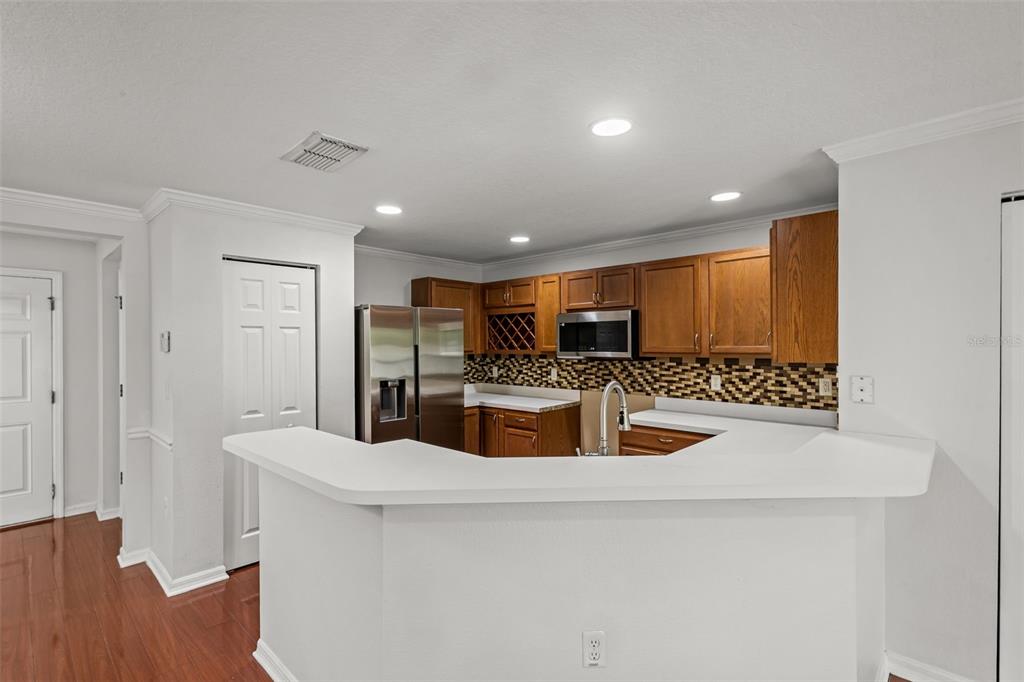 A kitchen features wood cabinets, stainless steel appliances, a tile backsplash, and dark wood flooring — 2972 ROYAL TUSCAN LANE, VALRICO, FL