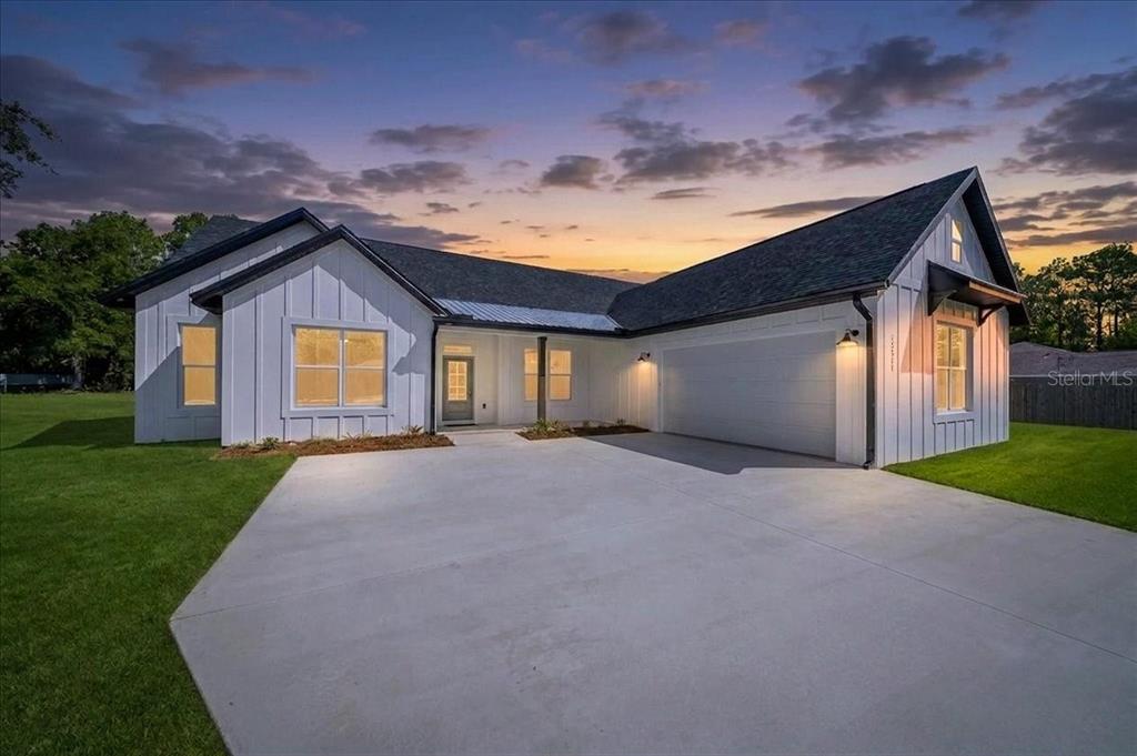 A white farmhouse-style house with a dark roof and a concrete driveway at dusk — 13511 SW 64TH ST ROAD, OCALA, FL