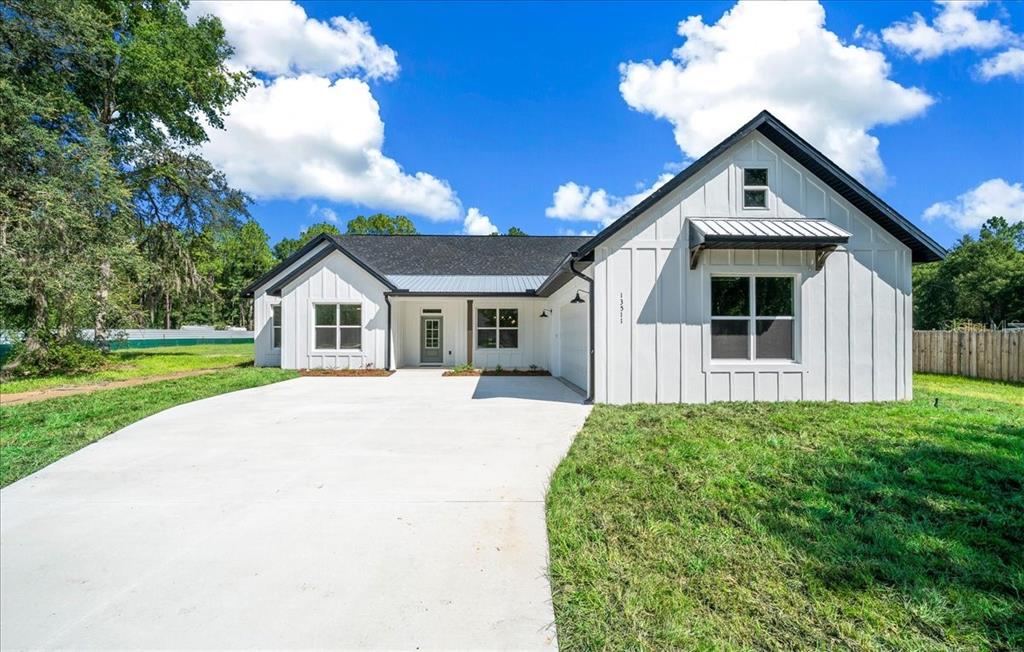 A single-story white farmhouse with black trim and a concrete driveway under a blue sky — 13511 SW 64TH ST ROAD, OCALA, FL
