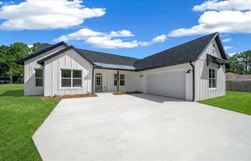 A modern white farmhouse with a black roof, board-and-batten siding, and a concrete driveway — 13511 SW 64TH ST ROAD, OCALA, FL