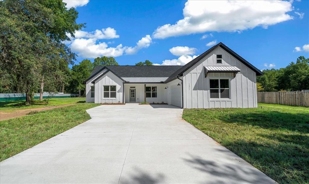 A white farmhouse-style home with a black roof and a large concrete driveway — 13511 SW 64TH ST ROAD, OCALA, FL