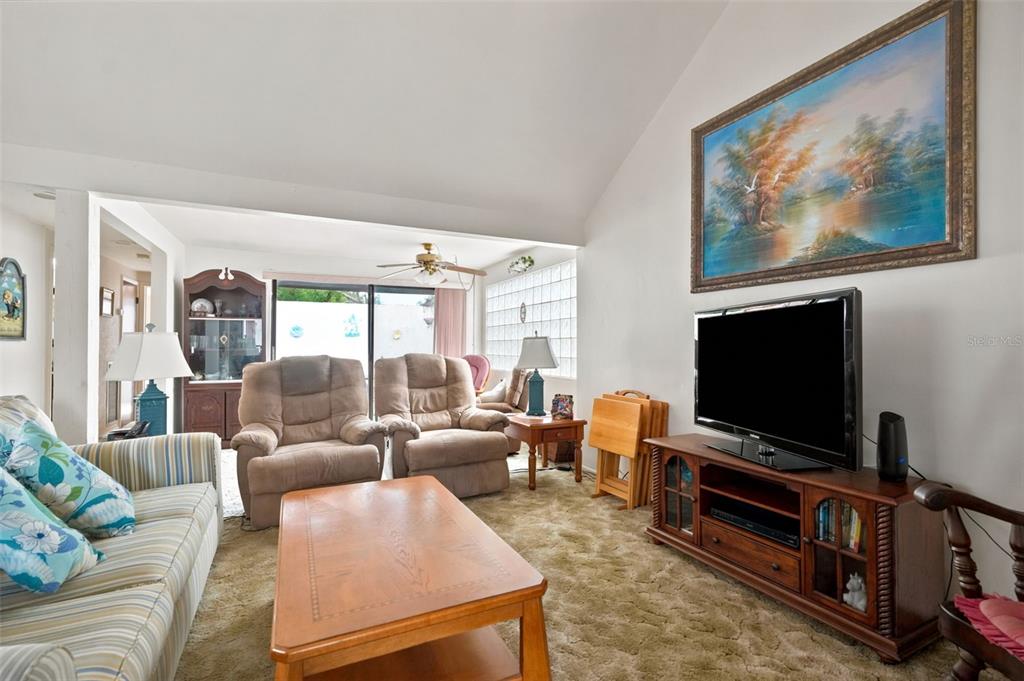 A living room features a striped sofa, two recliners, a television, and a large landscape painting — 7835 FOX DEN ROW, HUDSON, FL