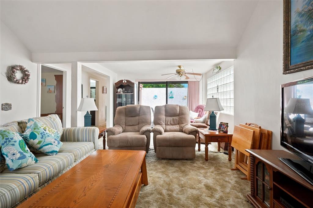 A living room features a striped sofa, two recliners, a coffee table, and glass block windows — 7835 FOX DEN ROW, HUDSON, FL