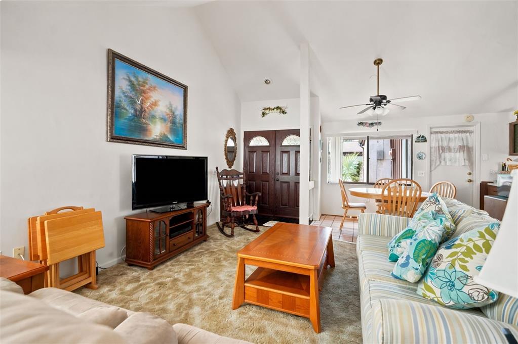 A living room features a vaulted ceiling, carpeted flooring, a television, and a wooden rocking chair — 7835 FOX DEN ROW, HUDSON, FL