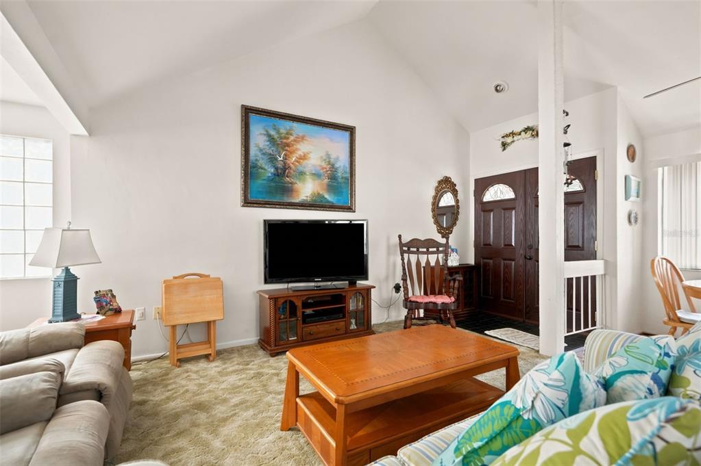 A living room features a vaulted ceiling, carpeted flooring, a television console, and a coffee table — 7835 FOX DEN ROW, HUDSON, FL