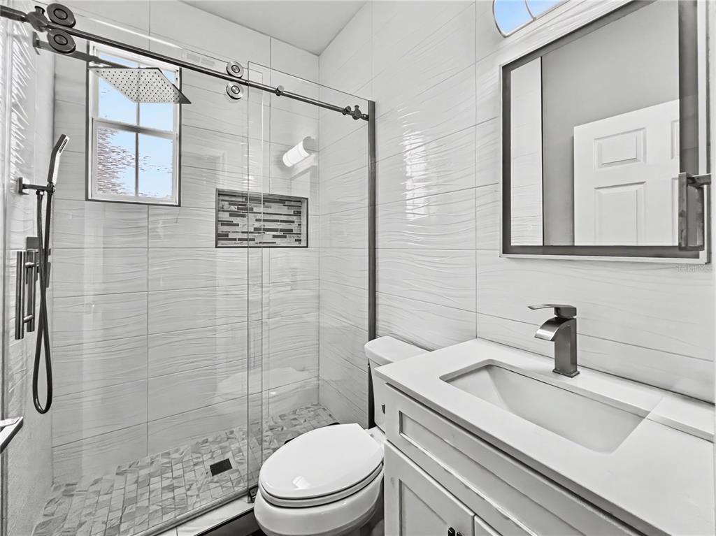 A modern bathroom features a glass-enclosed shower, a white vanity, and textured wall tiles — 839 LAKE EVALYN DRIVE, CELEBRATION, FL