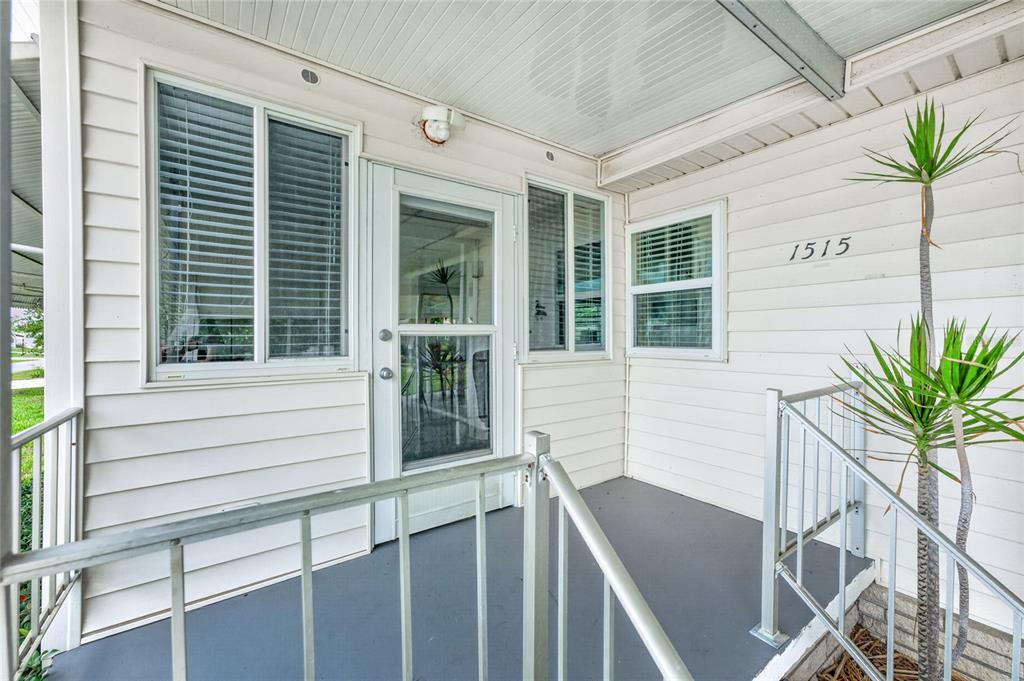 A covered front porch with light siding, a glass storm door, and metal railings — 1515 SANDERLING DRIVE, ENGLEWOOD, FL