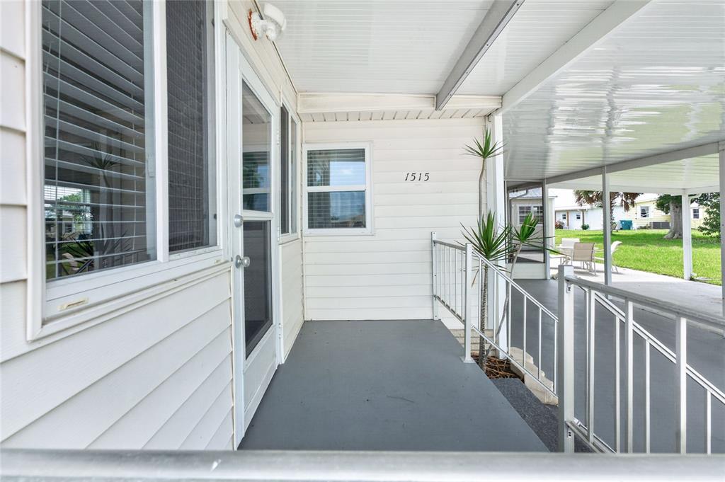 A covered porch with white siding, a glass door, and metal railings leads to an entrance — 1515 SANDERLING DRIVE, ENGLEWOOD, FL