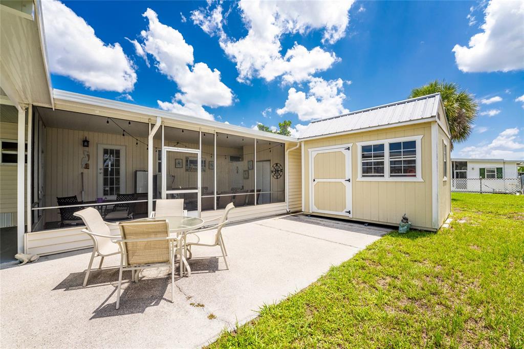 A patio with outdoor furniture sits beside a screened-in porch and a small storage shed — 1515 SANDERLING DRIVE, ENGLEWOOD, FL