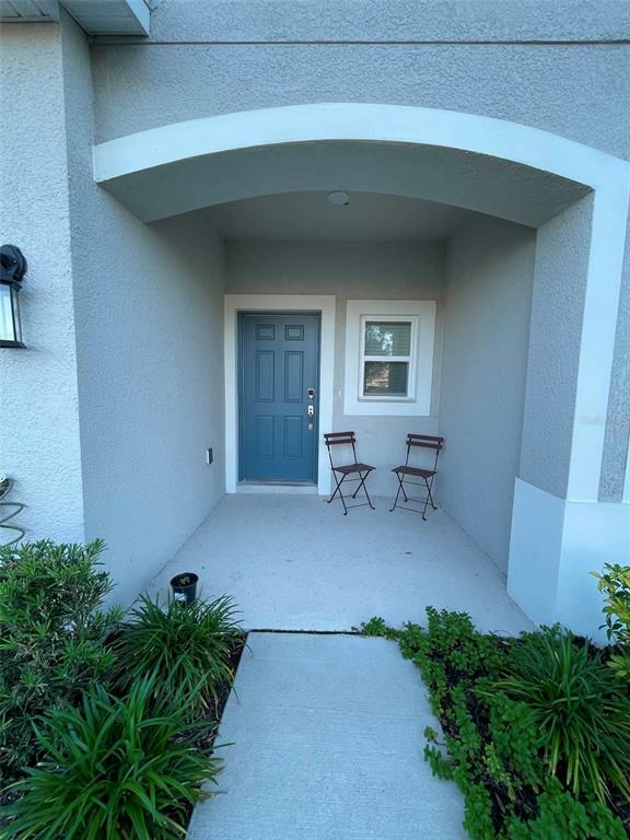 A covered entryway features a blue front door, a window, and two metal folding chairs — 2516 PARAVANE WAY, WESLEY CHAPEL, FL