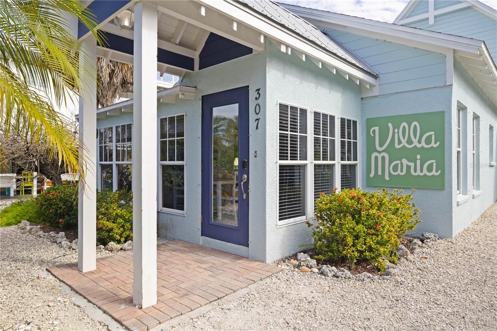 The exterior of a light blue building features a brick entryway and a prominent sign — 307 SPRING AVENUE, ANNA MARIA, FL