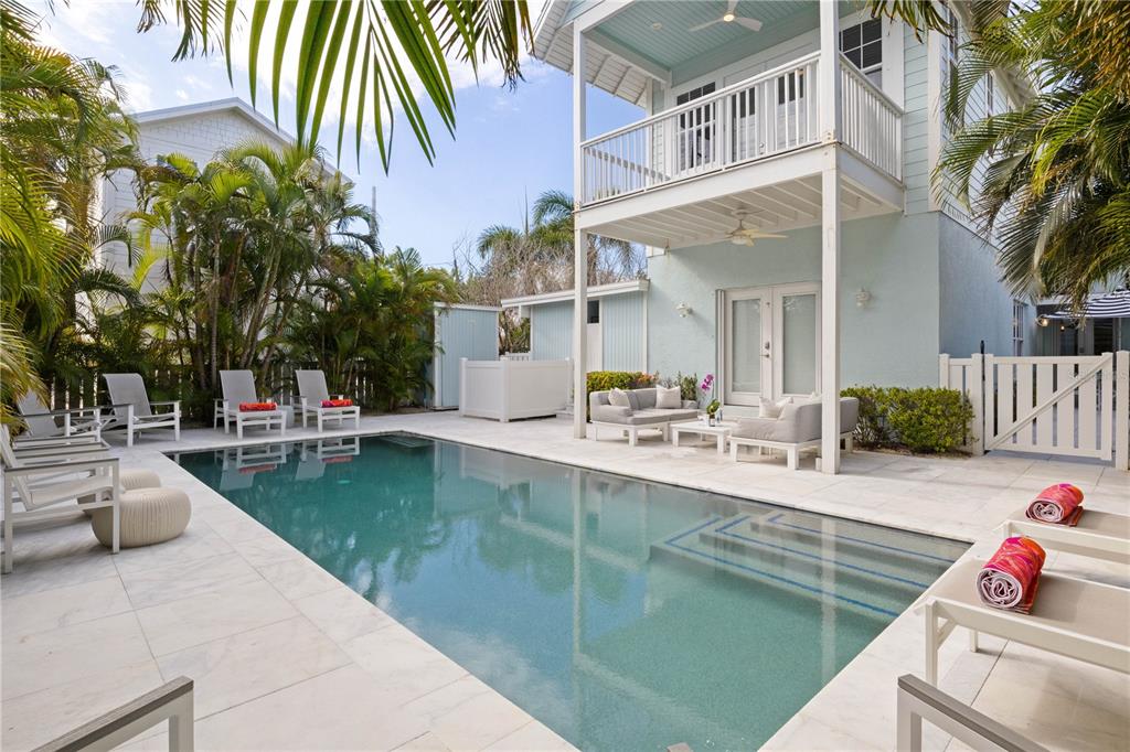 A swimming pool sits on a stone patio next to a two-story light blue house — 307 SPRING AVENUE, ANNA MARIA, FL