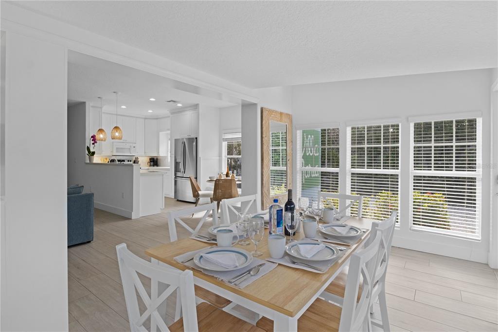 A dining area with a wooden table and white chairs opens into a modern white kitchen — 307 SPRING AVENUE, ANNA MARIA, FL