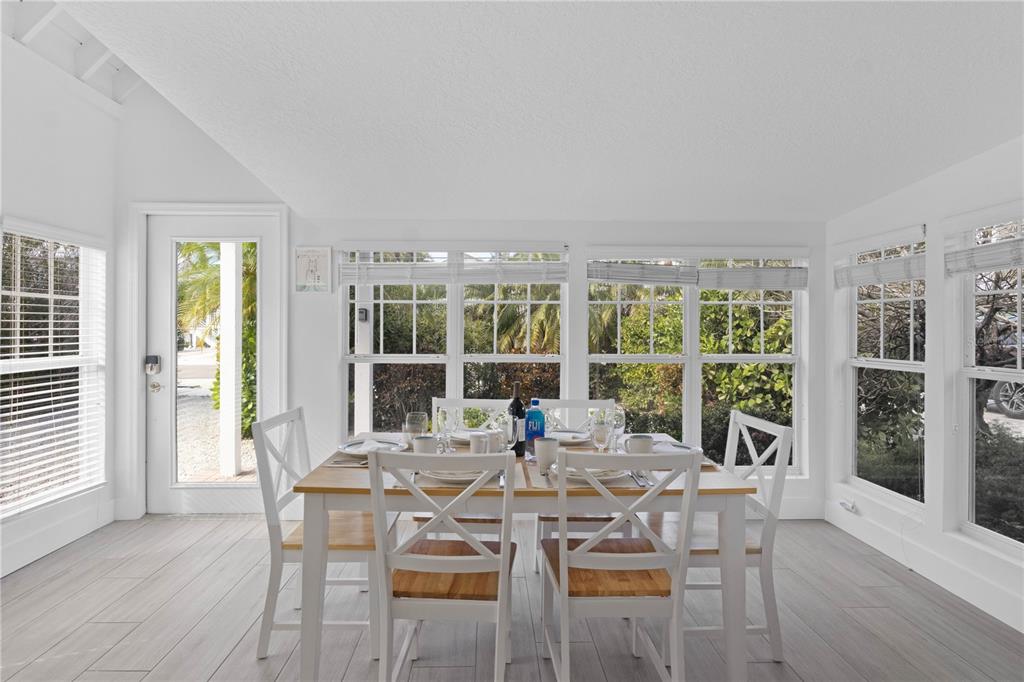 A bright dining room features a wooden table, white chairs, and large windows with blinds — 307 SPRING AVENUE, ANNA MARIA, FL