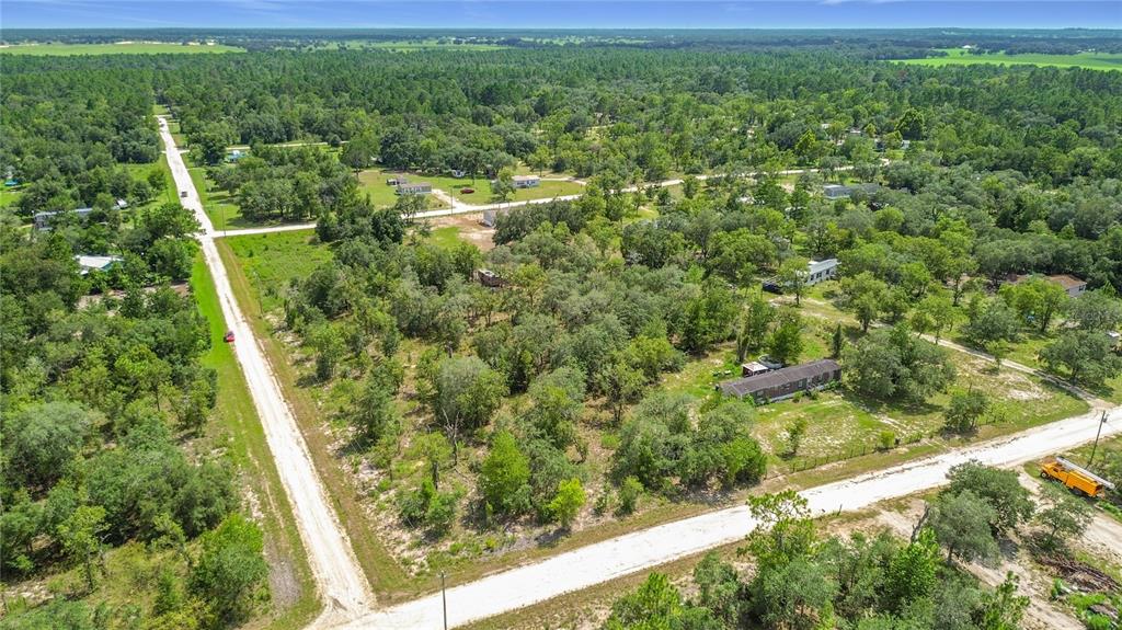 An aerial view shows a rural residential area with dirt roads, trees, and scattered houses — 0 SE 68TH TERRACE, MORRISTON, FL