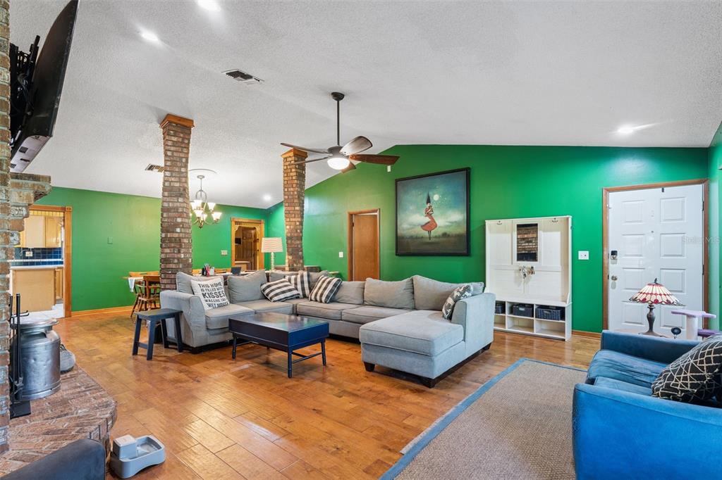 A living room with green walls, brick columns, hardwood floors, and a large sectional sofa — 15749 ARABIAN WAY, MONTVERDE, FL