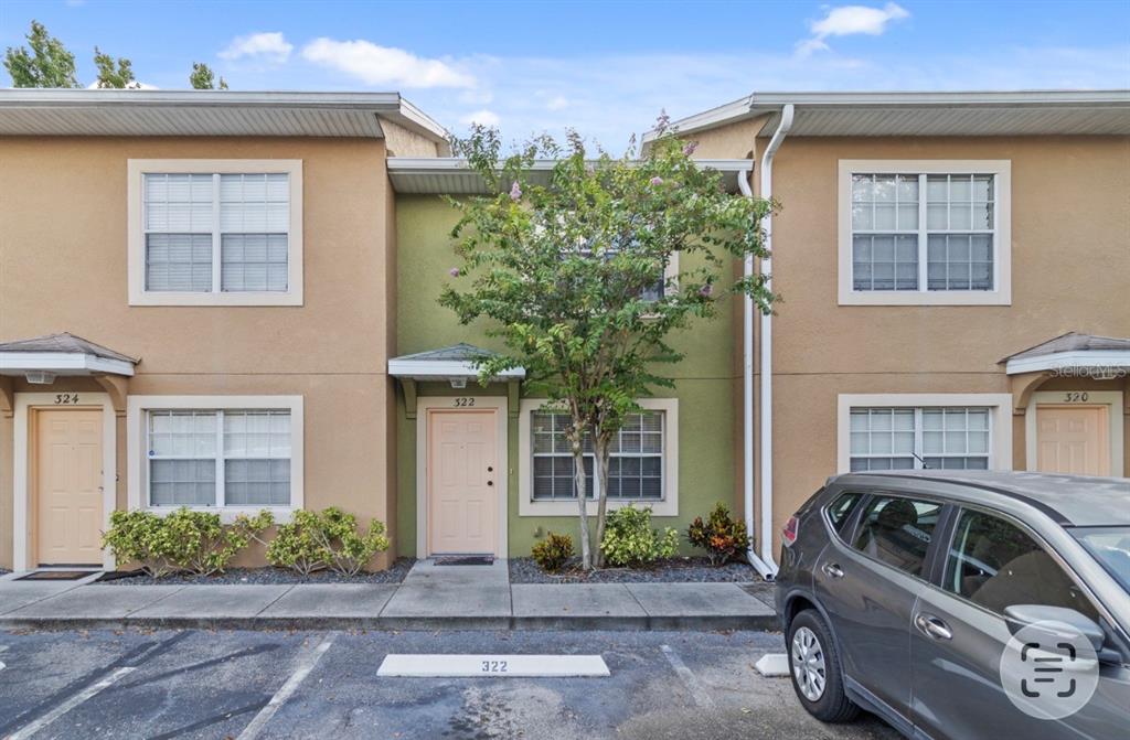 A two-story townhouse exterior with a green center unit, beige side units, and parking spaces — 322 CERVANTES DRIVE, KISSIMMEE, FL