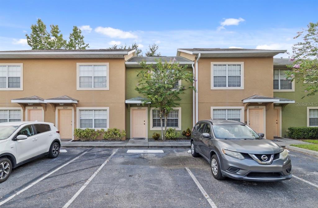 A row of two-story townhomes with tan stucco exteriors and parked cars in the foreground — 322 CERVANTES DRIVE, KISSIMMEE, FL