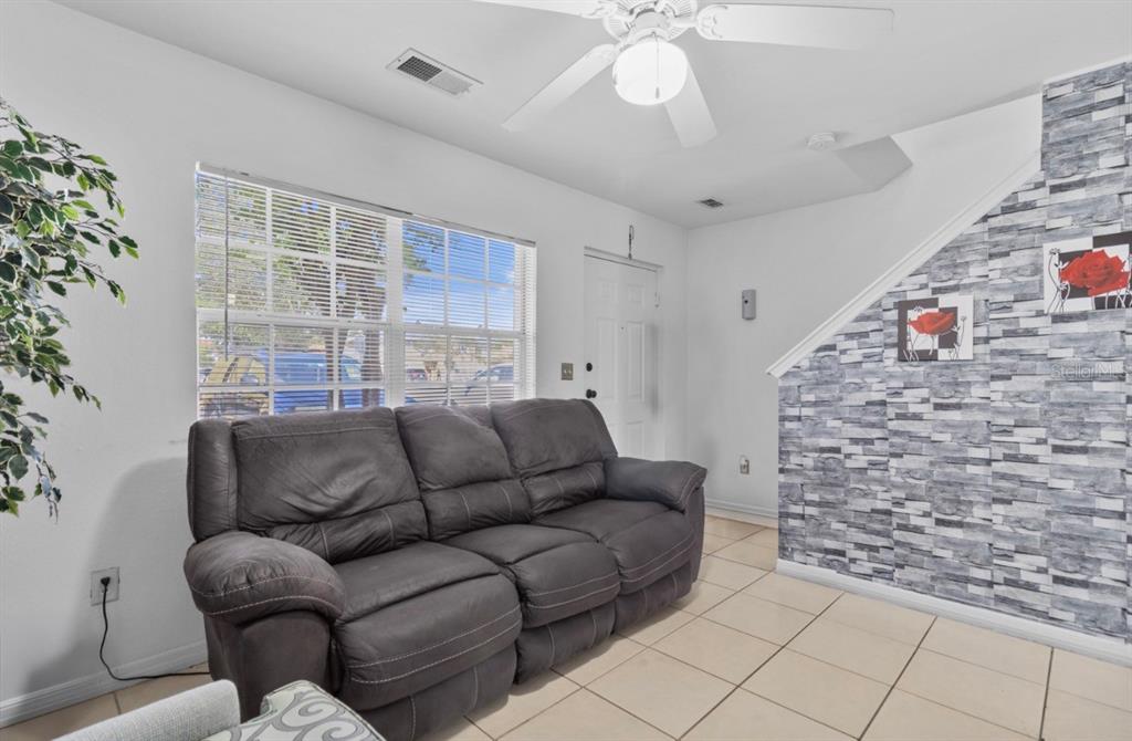 A living room features a gray reclining sofa, tiled floors, and a stone-patterned accent wall — 322 CERVANTES DRIVE, KISSIMMEE, FL