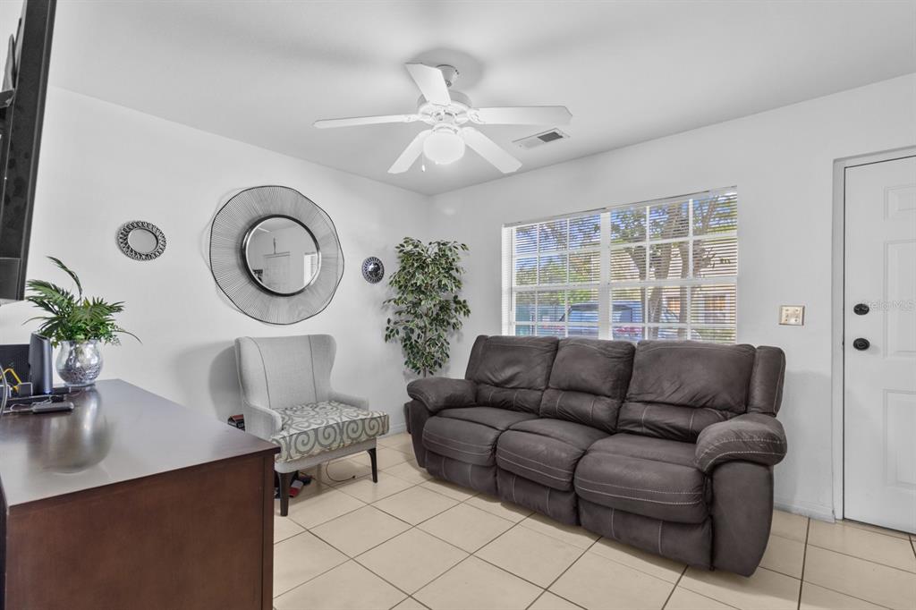 A living room features a dark gray sofa, an accent chair, tile flooring, and a ceiling fan — 322 CERVANTES DRIVE, KISSIMMEE, FL
