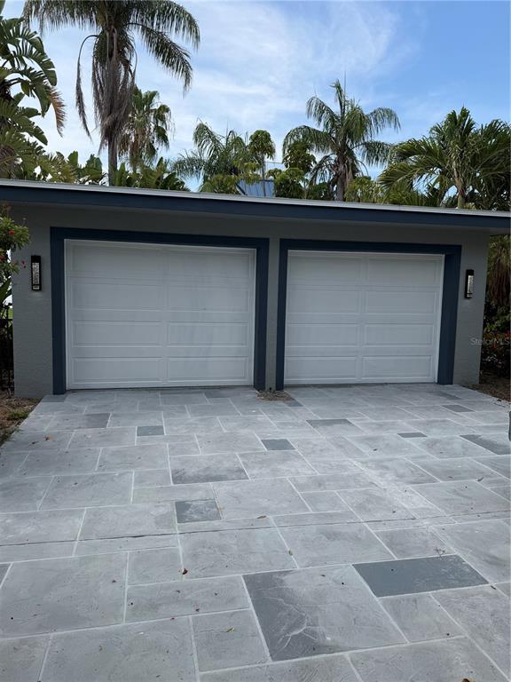 A two-car garage with white doors and a gray stone-patterned driveway under palm trees — 887 S GULFVIEW BOULEVARD, CLEARWATER BEACH, FL