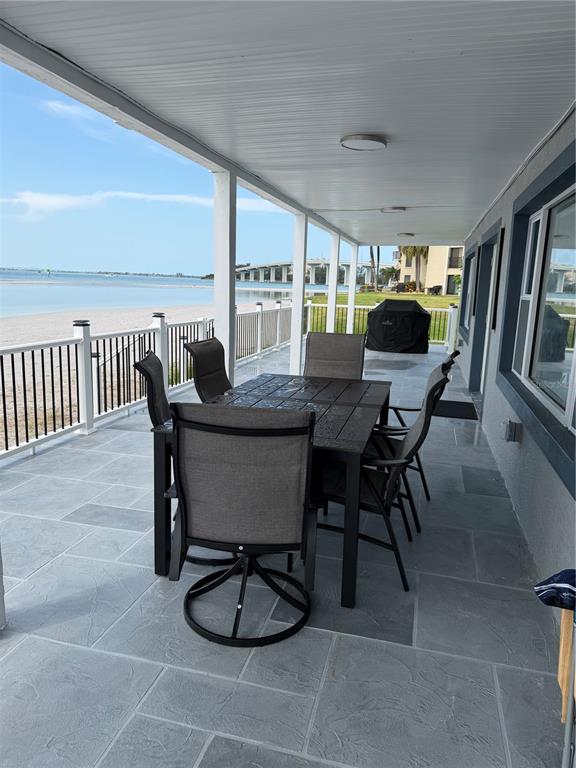 A covered patio features a dining set, stone-look tile flooring, and a view of water — 887 S GULFVIEW BOULEVARD, CLEARWATER BEACH, FL