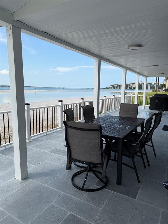A covered patio with a dining set overlooks a sandy beach and a distant bridge — 887 S GULFVIEW BOULEVARD, CLEARWATER BEACH, FL