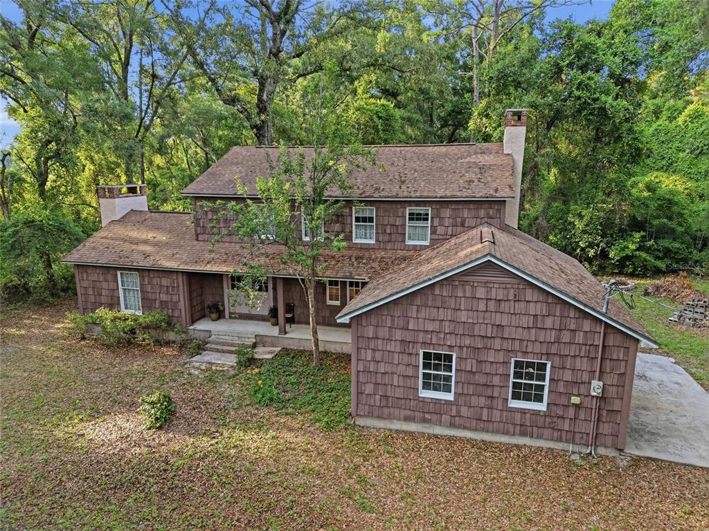 An elevated view of a two-story brown shingle house with a large wooden deck — 9291 NW 127TH PLACE, CHIEFLAND, FL