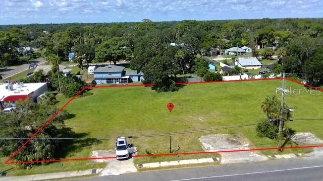 An aerial view shows a vacant, grassy lot outlined in red with a parked white vehicle — 2606 N DIXIE FREEWAY, NEW SMYRNA BEACH, FL