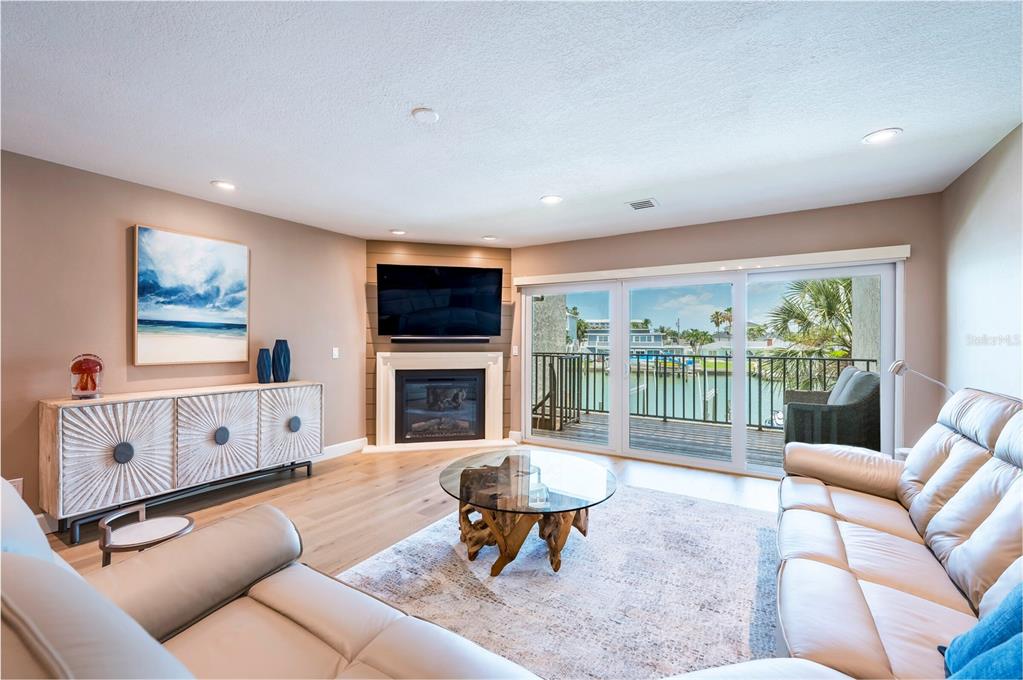 A living room features a corner fireplace, a glass-topped coffee table, and sliding doors to a balcony — 218 SKIFF POINT, CLEARWATER BEACH, FL