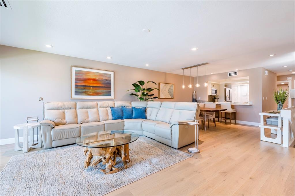 A living room features a large beige sectional sofa, a glass-topped driftwood coffee table, and hardwood floors — 218 SKIFF POINT, CLEARWATER BEACH, FL