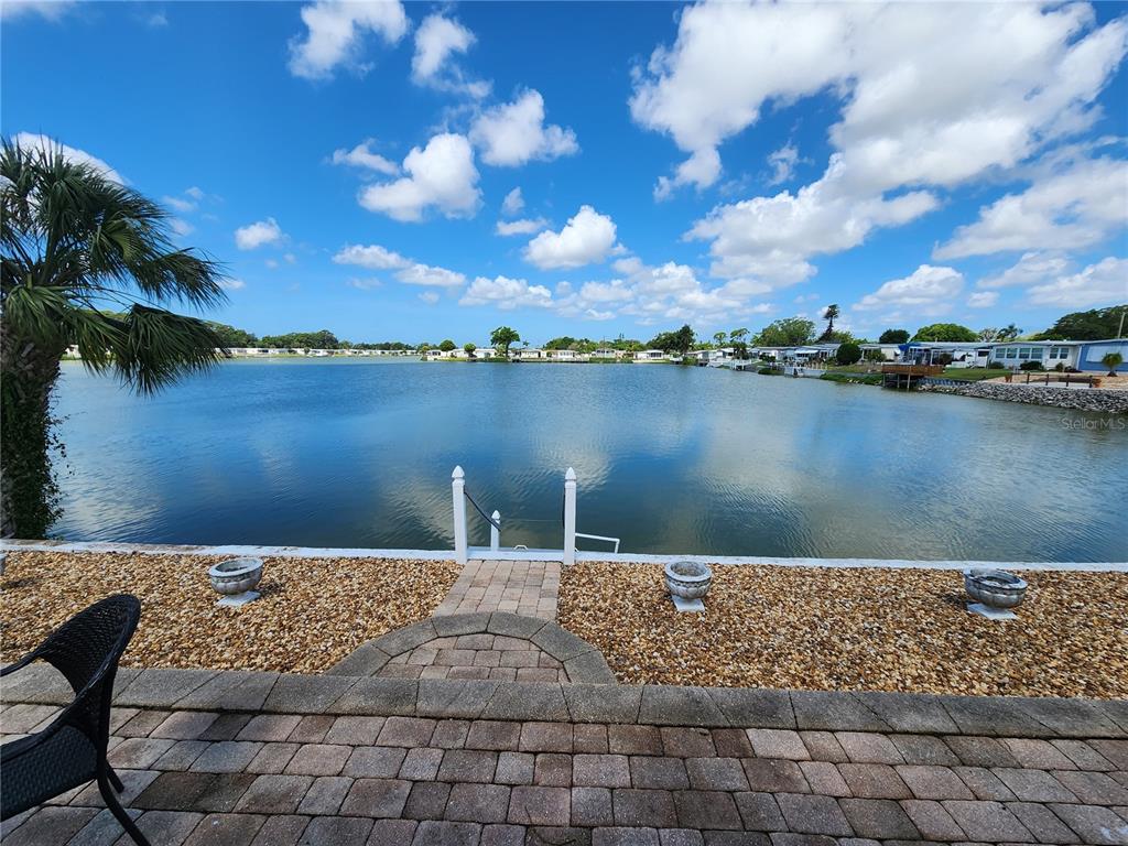 A stone patio overlooks a lake with a small dock and surrounding mobile homes — 808 53RD AVENUE E UNIT 27, BRADENTON, FL