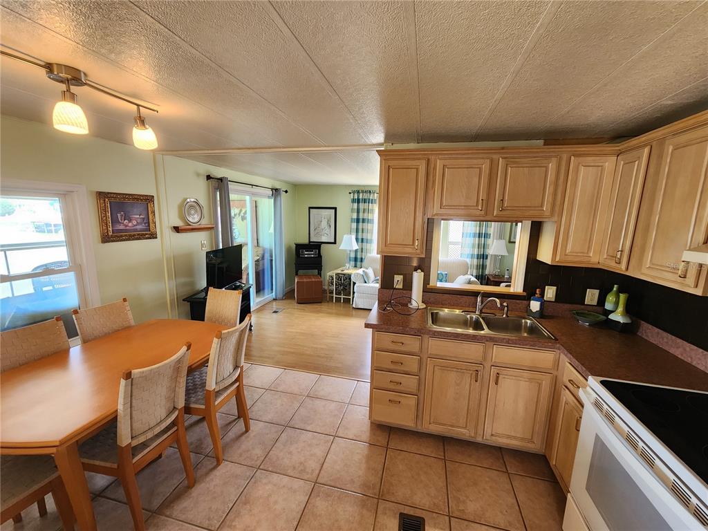 A kitchen with light wood cabinets and tile floors opens into a dining and living area — 808 53RD AVENUE E UNIT 27, BRADENTON, FL