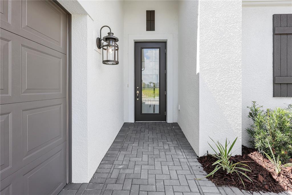 A paved walkway leads to a dark-framed glass front door beside a gray garage door — 14366 HAMMOCK OAK STREET, PARRISH, FL