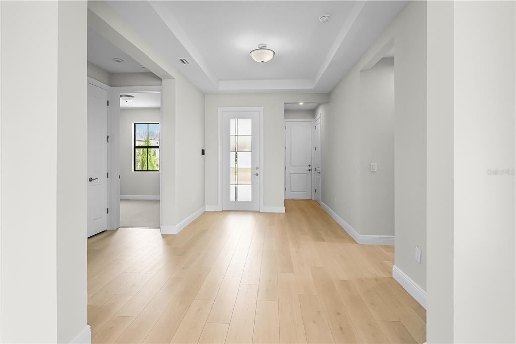 A bright entryway features light wood flooring, a tray ceiling, and a glass-paneled front door — 14366 HAMMOCK OAK STREET, PARRISH, FL