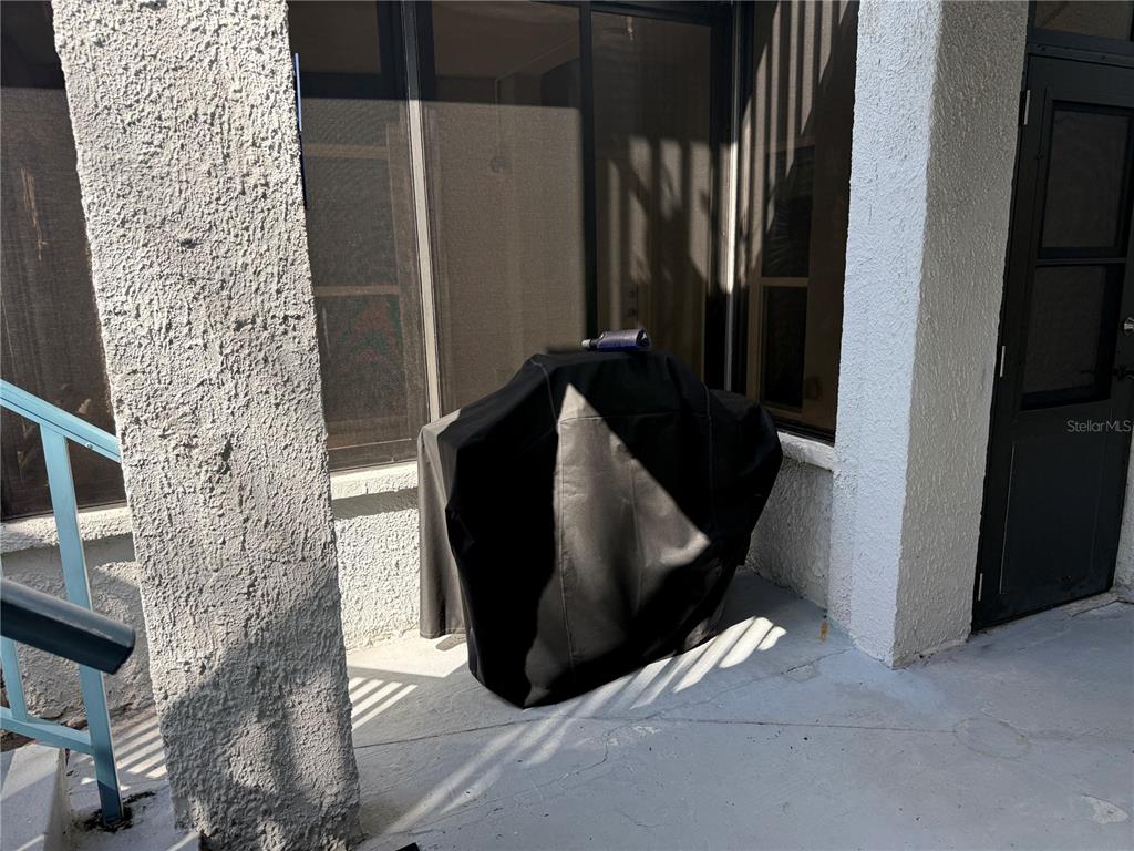 A covered grill sits on a concrete patio next to a sliding glass door — 179 MEDALLION BOULEVARD UNIT D, MADEIRA BEACH, FL