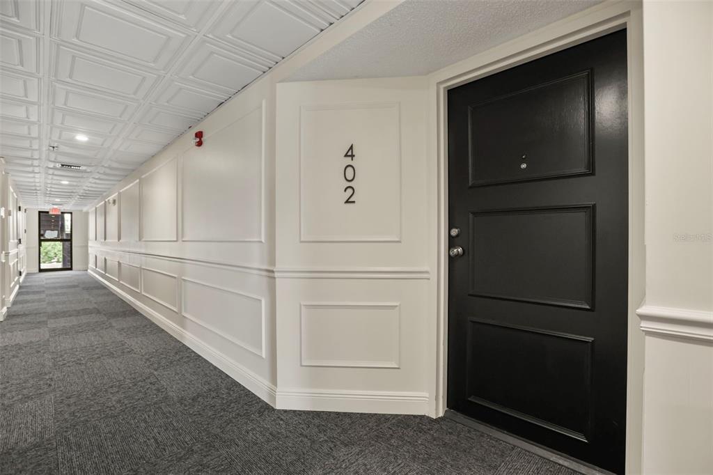 A hallway with gray carpet, white paneled walls, a coffered ceiling, and a black door — 300 CAROLINA AVENUE UNIT 402C, WINTER PARK, FL