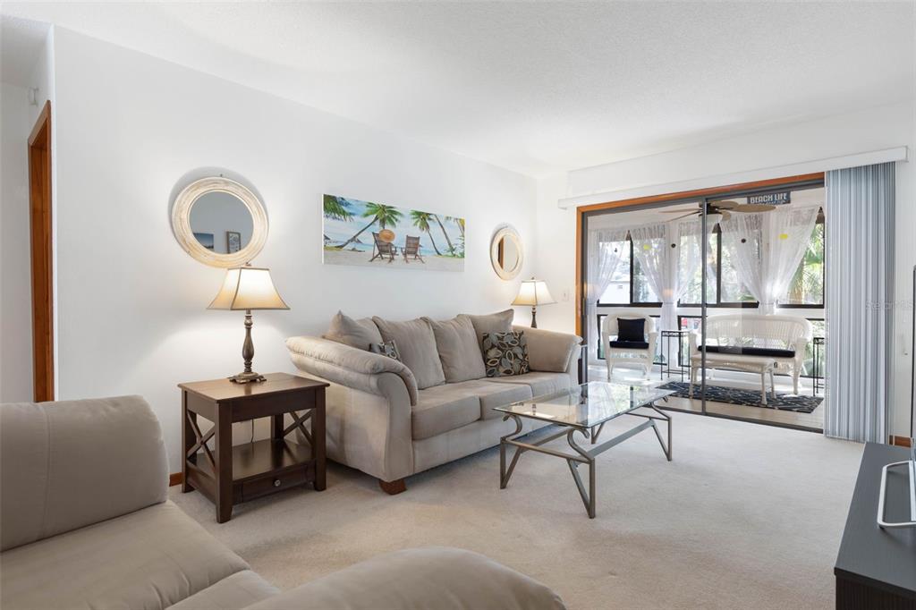 A living room features a beige sofa, glass coffee table, and a sliding door to a balcony — 24 FAIRWAYS CIRCLE UNIT 24, PALM COAST, FL