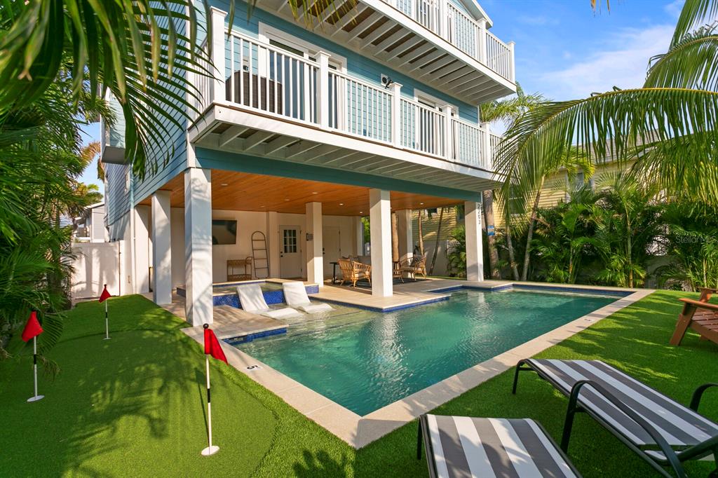 A stilted house with a backyard pool, putting green, and lounge chairs on artificial turf — 2203 AVENUE B, BRADENTON BEACH, FL