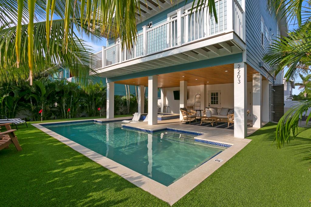 A blue stilt house features a swimming pool, covered patio, and artificial turf lawn — 2203 AVENUE B, BRADENTON BEACH, FL