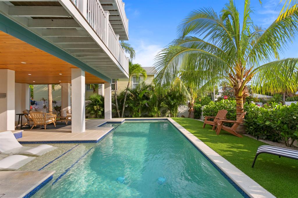 A swimming pool with a tanning ledge sits beside a covered patio and palm trees — 2203 AVENUE B, BRADENTON BEACH, FL