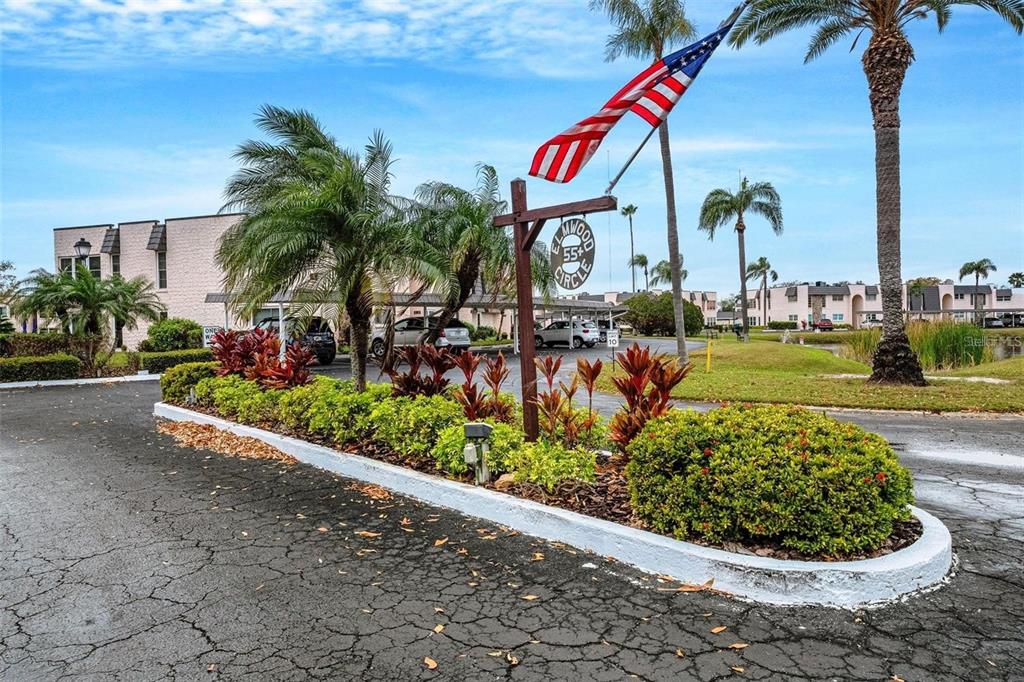 A sign for a 55+ community stands in a landscaped island with palm trees — 112 ELMWOOD CIRCLE UNIT 112, SEMINOLE, FL