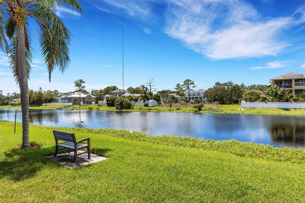 A park bench sits on a grassy lawn overlooking a pond with houses in the background — 112 ELMWOOD CIRCLE UNIT 112, SEMINOLE, FL