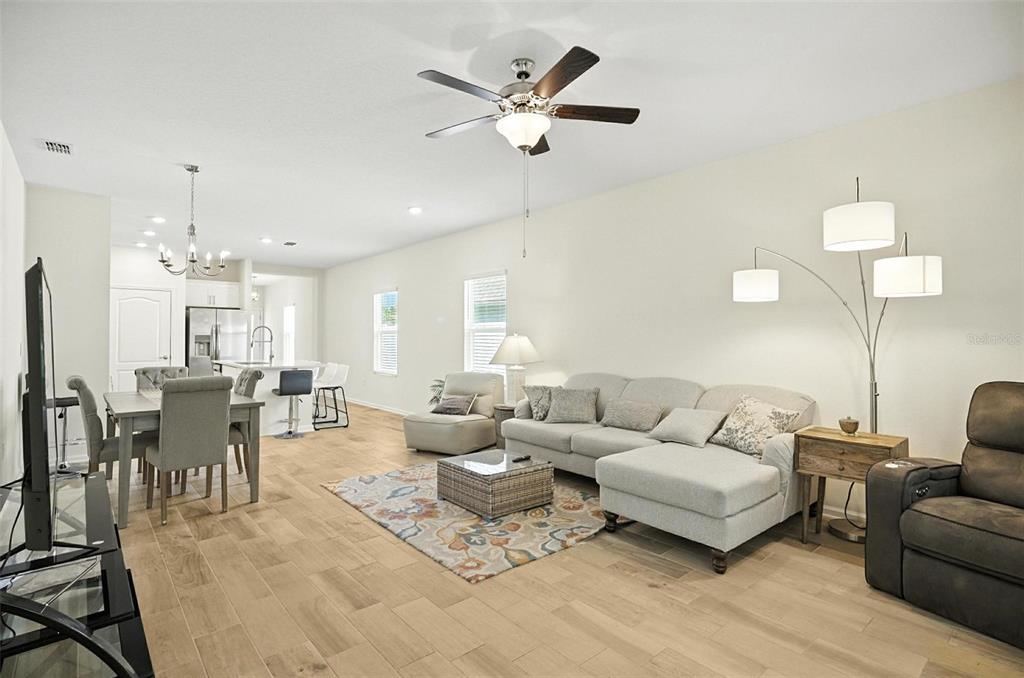 An open-concept living and dining area features light wood flooring, a sectional sofa, and kitchen — 88 BIRDIE WAY, BUNNELL, FL
