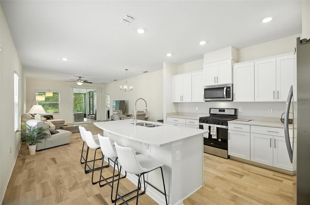 A bright, open-concept kitchen features white cabinetry, a central island with seating, and light flooring — 88 BIRDIE WAY, BUNNELL, FL