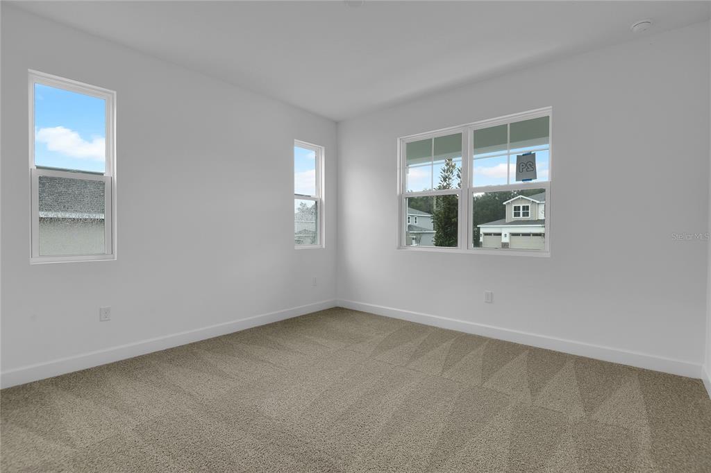 An empty bedroom features light gray walls, beige carpeting, and three windows overlooking a neighborhood — 741 WEKIVA RIDGE DRIVE, MOUNT DORA, FL