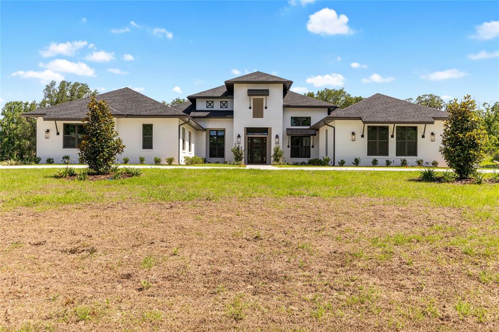 A white modern farmhouse with a dark roof and large windows sits on a lawn — 950 SE 80TH STREET, OCALA, FL